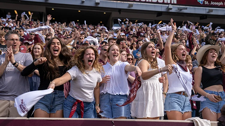 Excited Texas A&M students cheer and wave towels in a packed Kyle Field stadium following a touchdown during an Aggies football game.
