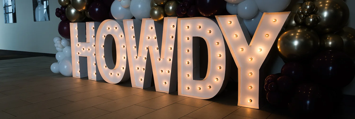 Sign with interior lights spelling out HOWDY surrounded by balloons