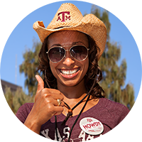 A woman makes the Gig'em thumbs up hand gesture. 