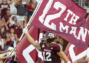 A Texas A&M Aggie's football player runs onto the field carrying a 12th man flag. 